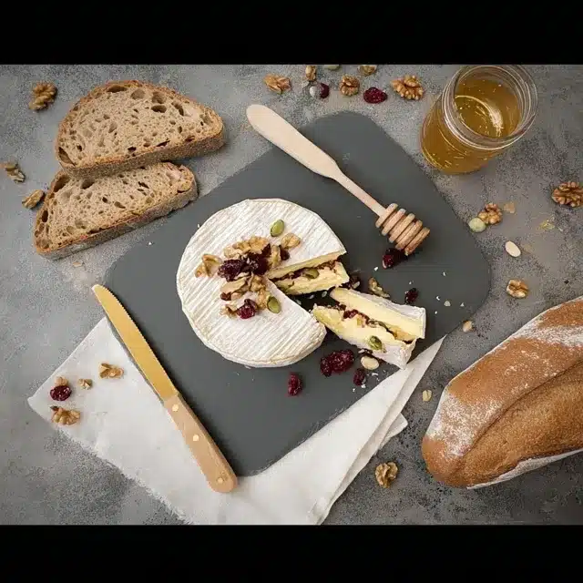 Un camembert farci aux noix et aux cranberries, joliment présenté sur une ardoise avec du pain et du miel.
