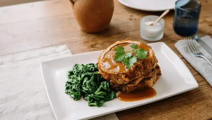 Tranche de Bœuf Wellington doré avec sa sauce et des légumes verts, présentée sur une table en bois rustique