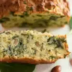 Un pain salé moelleux garni de feuilles de chou vertes et d'ammandes blanchies, présenté sur une assiette blanche.